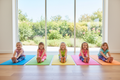 Five girls doing seated forward fold yoga pose on colorful mats in a bright studio